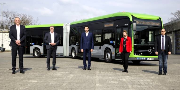 Drei Männer und eine Frau stehen vor einem Bus.